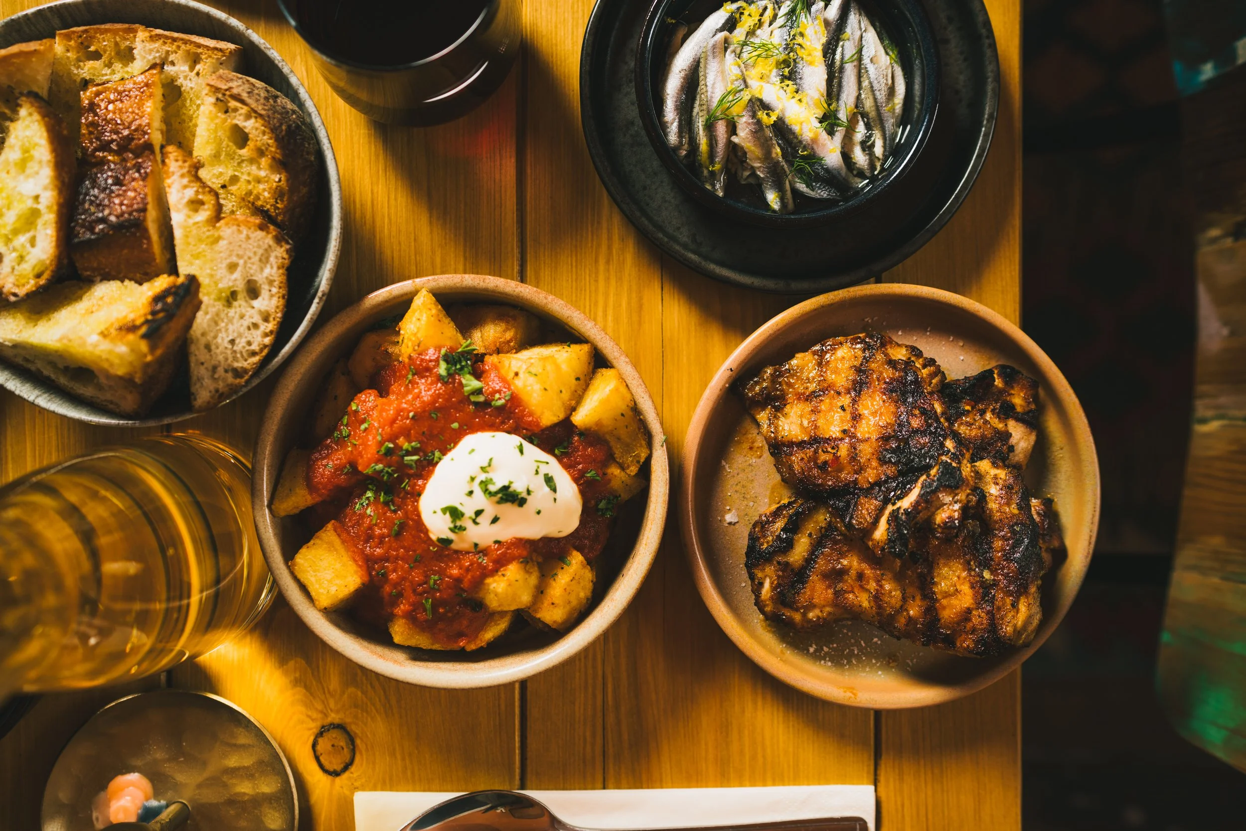 Overhead view of shared Portuguese dishes — grilled chicken, patatas bravas, anchovies and bread